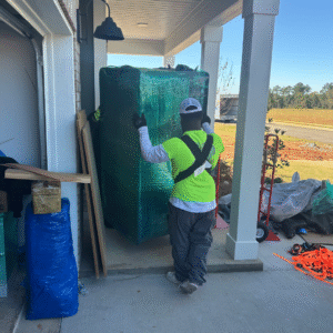 Two professional movers from The Moving Guys carefully maneuver a large, wrapped gun safe through a front porch entryway during a move in the Wiregrass area.